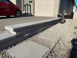 A well-constructed hardscape featuring a sturdy retaining wall and stepping stones leading to a residence, with a focus on practicality and aesthetic appeal in a suburban setting.