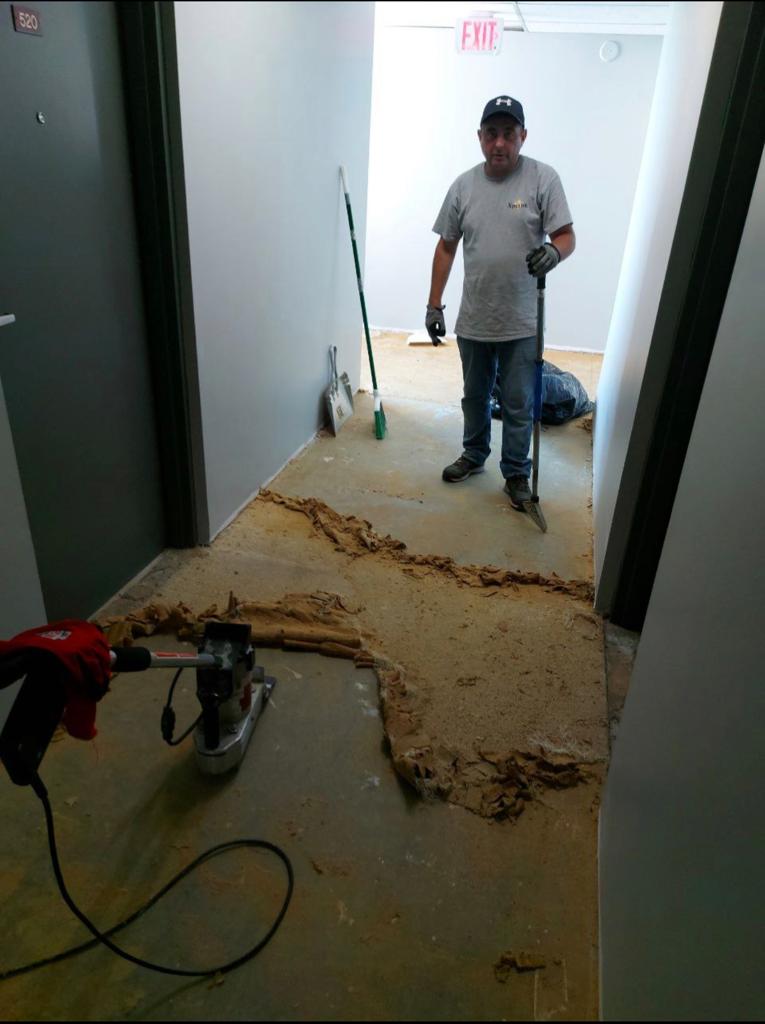 a construction worker near removed flooring nearby and a power tool on the ground, indicating an ongoing renovation or installation process.