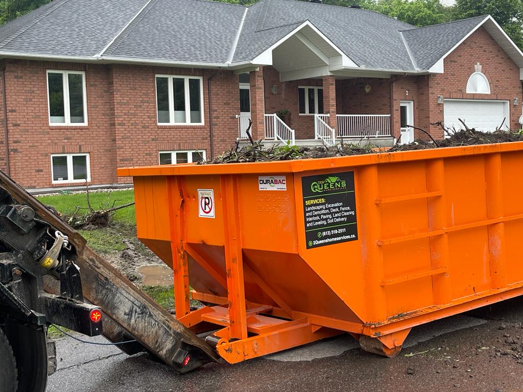 A vibrant orange Durabac dumpster filled with yard waste is positioned in front of a brick residential home, highlighting the cleanup phase of a landscaping project.