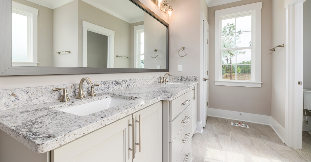 A finished bathroom interior with a long vanity featuring granite countertops and dual sinks with brushed nickel faucets