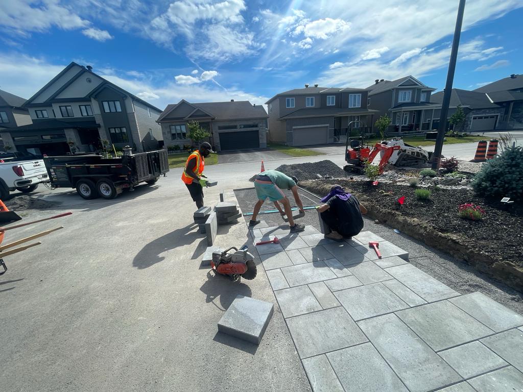 A team of professionals is meticulously laying down interlocking paving stones on a residential driveway.
