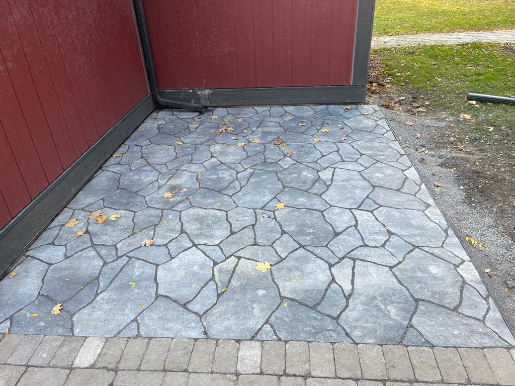 a close-up view of a gray flagstone interlocking pathway, bordered by a red wooden gate
