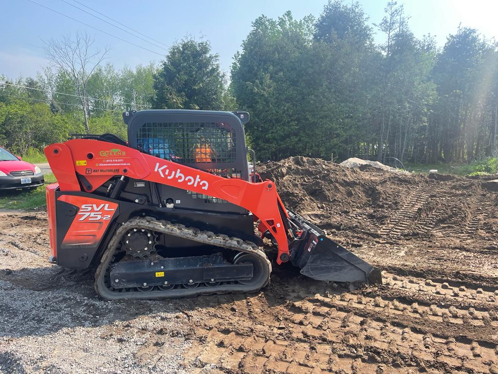 A red Kubota compact track loader is positioned on a construction site, with its bucket engaged in the ground.