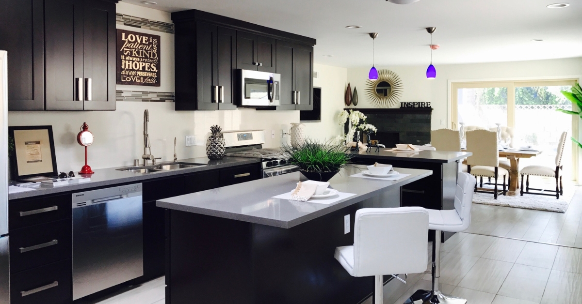 A stylish kitchen with dark cabinets and granite countertops, complemented by a breakfast bar with white stools. The open-concept layout transitions seamlessly into a cozy dining area with natural light filtering in, creating an inviting space for meals and gatherings