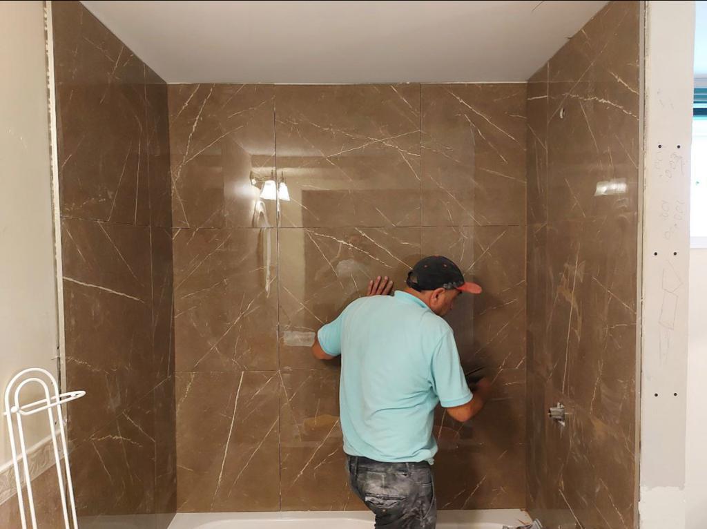 a skilled worker is meticulously installing large, marble-like tiles in a bathroom shower area, ensuring each piece is perfectly aligned
