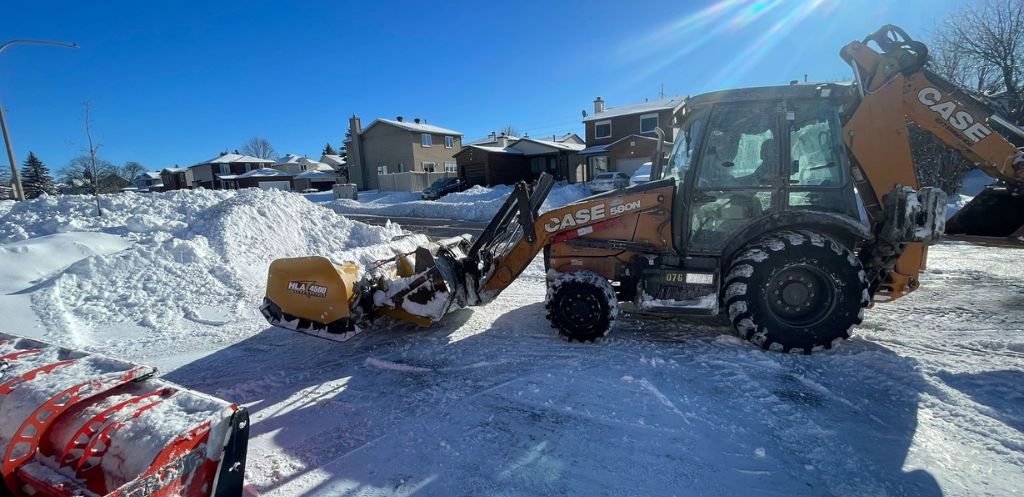 A CASE backhoe loader actively clears a snow-covered parking area, showcasing effective commercial snow removal services on a sunny day in a residential Ottawa neighborhood.