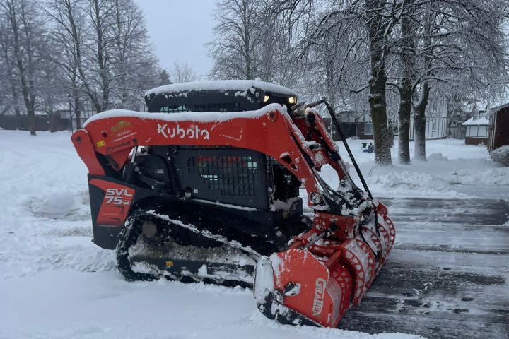 A red Kubota skid steer is actively plowing snow, demonstrating efficient snow management during a snowy day in Ottawa, ensuring clear pathways and safe surfaces