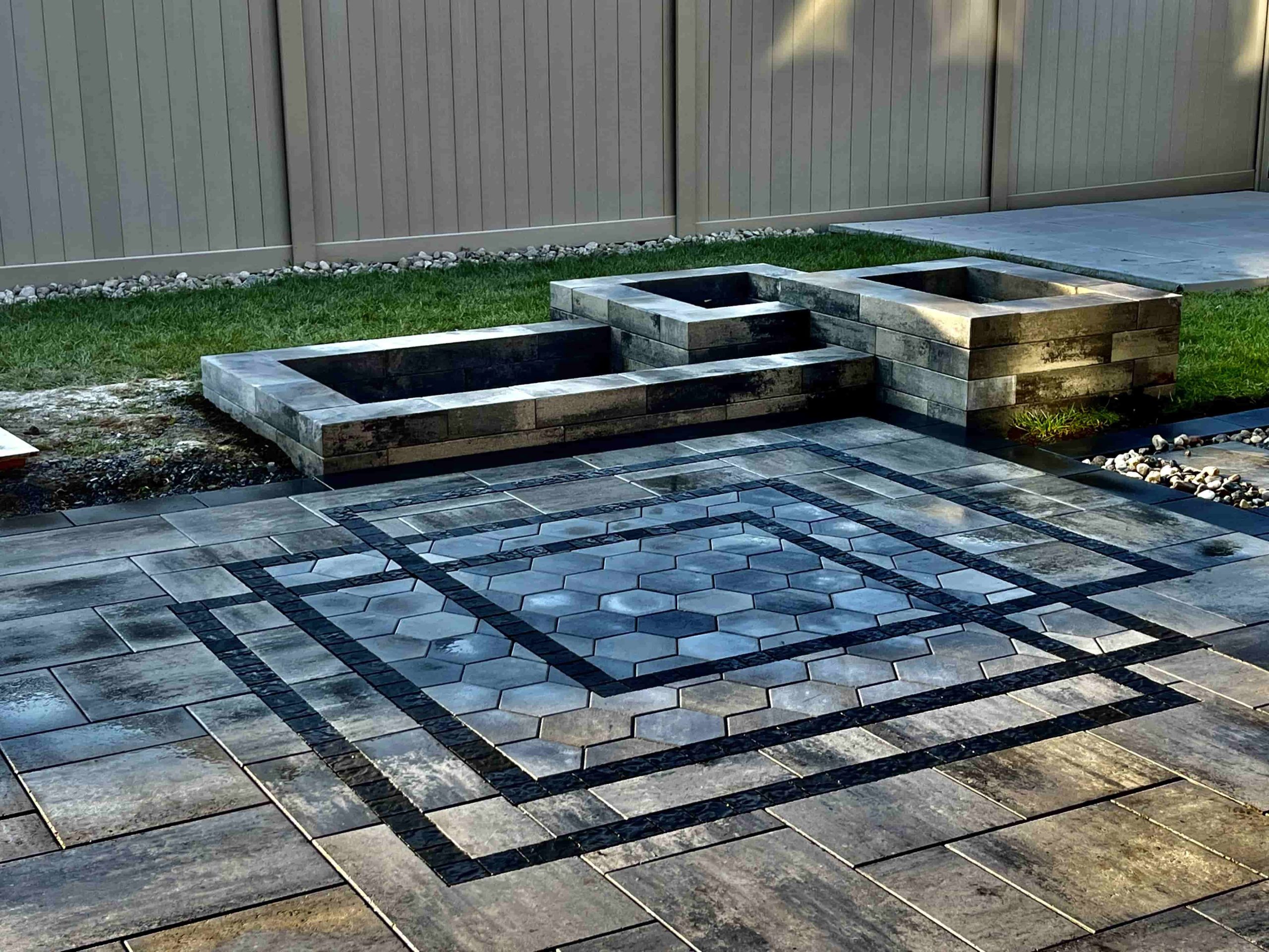 A meticulously designed patio with interlocking stones in a geometric pattern. The central area showcases hexagonal stones bordered by a double row of darker, contrasting stones, creating an elegant focal point.