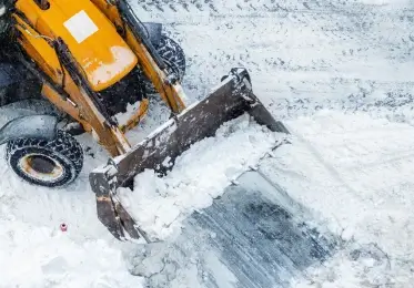 two queens home services yellow and black construction vehicle excavates snow